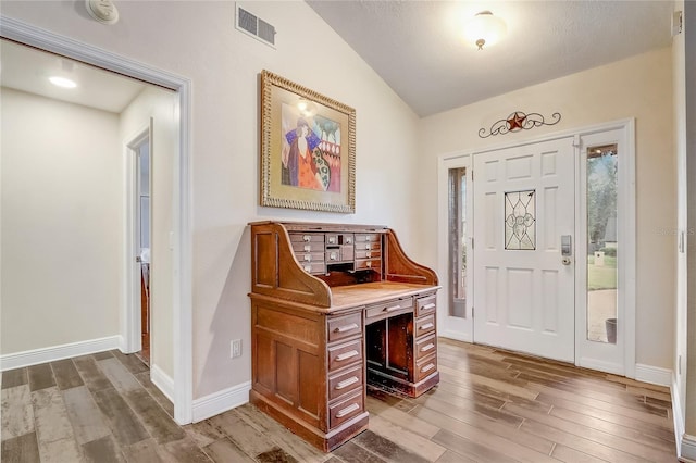 foyer with lofted ceiling, visible vents, baseboards, and wood finished floors