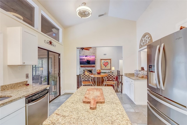 kitchen with light stone counters, visible vents, appliances with stainless steel finishes, a brick fireplace, and white cabinets