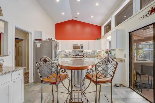 kitchen featuring high vaulted ceiling, light stone counters, white cabinets, appliances with stainless steel finishes, and tasteful backsplash