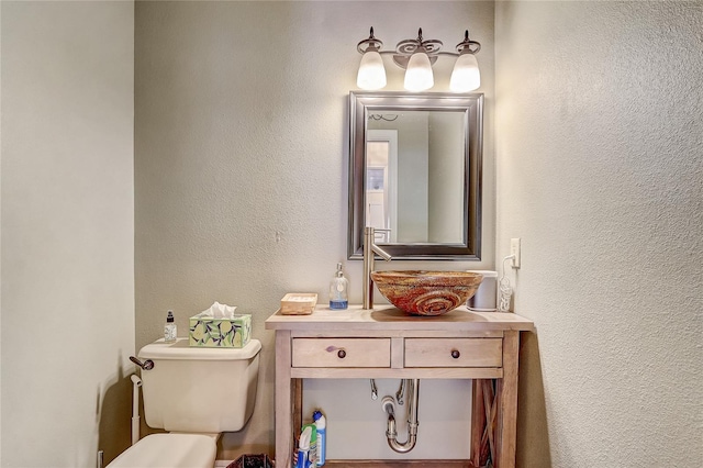 half bathroom featuring a textured wall, vanity, and toilet