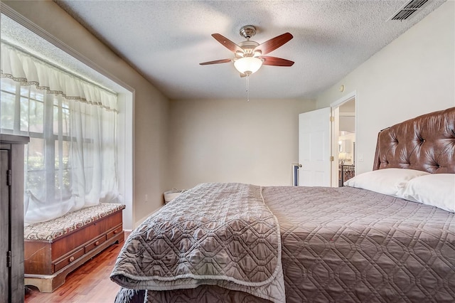 bedroom with light wood-style floors, ceiling fan, visible vents, and a textured ceiling