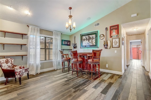 dining space with a dry bar, lofted ceiling, visible vents, wood finished floors, and baseboards