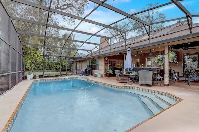 outdoor pool with glass enclosure, a patio area, and a ceiling fan