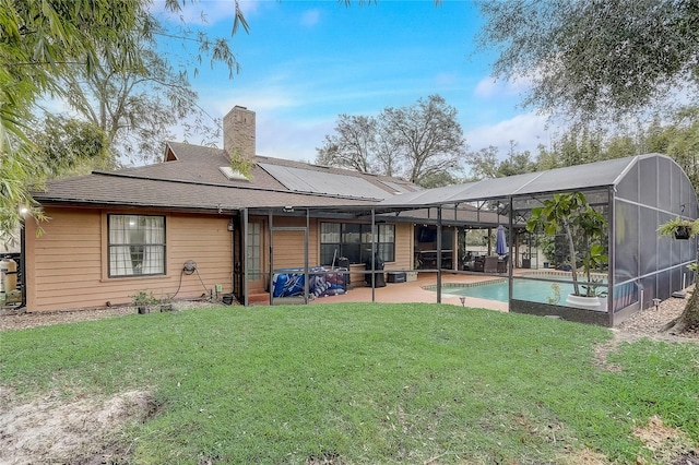 rear view of house featuring an outdoor pool, a lawn, glass enclosure, a chimney, and a patio area