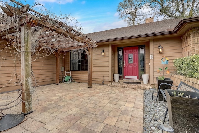 doorway to property with a patio area, a shingled roof, a chimney, and a pergola