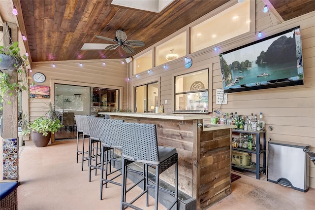 bar featuring a dry bar, vaulted ceiling, wooden walls, ceiling fan, and wooden ceiling