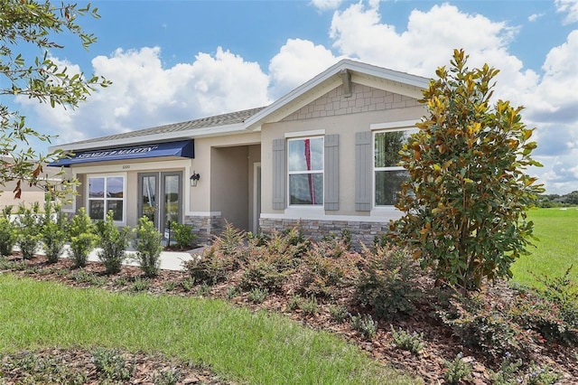 view of front of property with stone siding, a front yard, and stucco siding