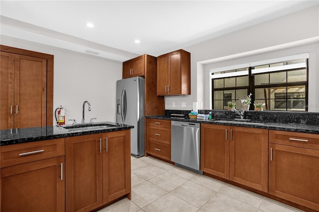 kitchen with stainless steel appliances, brown cabinetry, dark stone countertops, and a sink