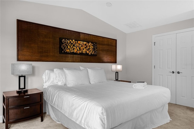 bedroom featuring a closet, light colored carpet, vaulted ceiling, and visible vents