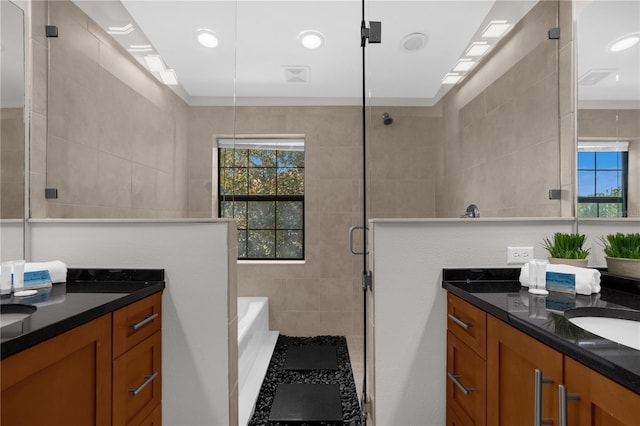 full bathroom featuring two vanities, a stall shower, a garden tub, and plenty of natural light