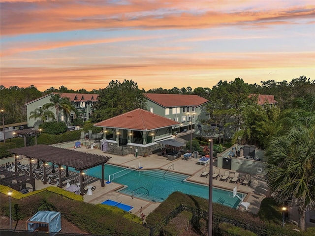 pool at dusk with outdoor dry bar, area for grilling, a patio area, a community pool, and a pergola