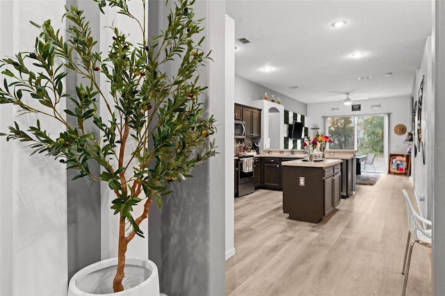 kitchen featuring a kitchen island with sink, stainless steel appliances, light countertops, dark brown cabinets, and light wood-style floors