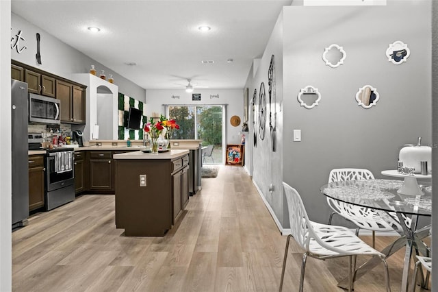 kitchen featuring a center island, light countertops, appliances with stainless steel finishes, light wood-style floors, and dark brown cabinetry