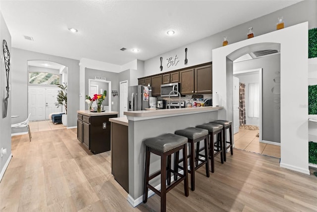 kitchen with arched walkways, dark brown cabinetry, visible vents, light countertops, and appliances with stainless steel finishes