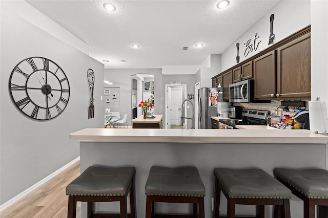 kitchen with stainless steel appliances, light countertops, dark brown cabinetry, and a peninsula