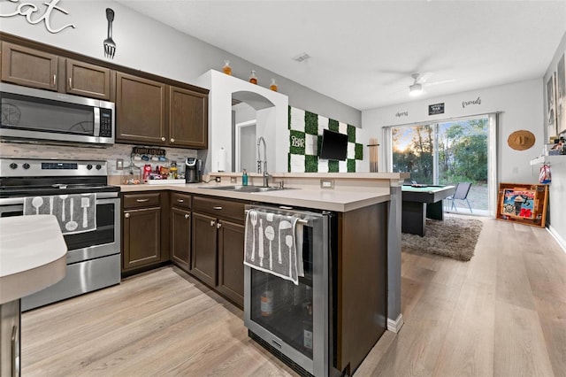 kitchen featuring wine cooler, light countertops, appliances with stainless steel finishes, a sink, and dark brown cabinets