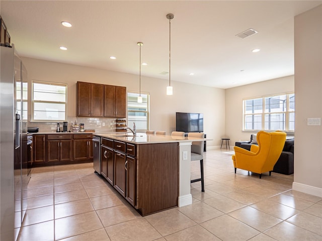 kitchen featuring open floor plan, a kitchen island with sink, stainless steel appliances, light countertops, and pendant lighting