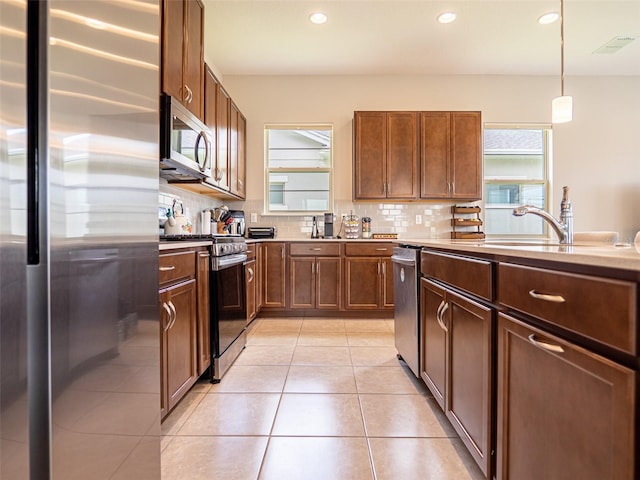 kitchen with light tile patterned floors, stainless steel appliances, visible vents, hanging light fixtures, and tasteful backsplash