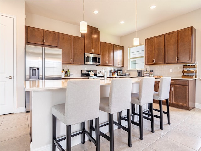 kitchen with stainless steel appliances, pendant lighting, light countertops, and a center island with sink