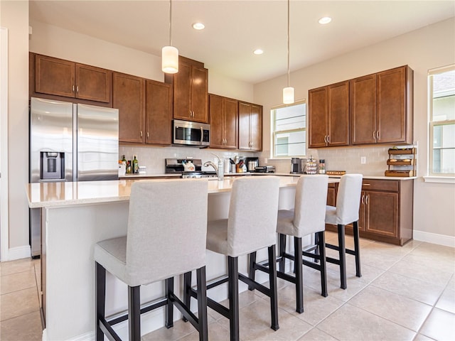 kitchen featuring appliances with stainless steel finishes, light countertops, a center island with sink, and hanging light fixtures