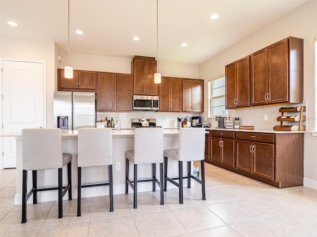 kitchen featuring a breakfast bar area, a kitchen island with sink, light countertops, appliances with stainless steel finishes, and pendant lighting