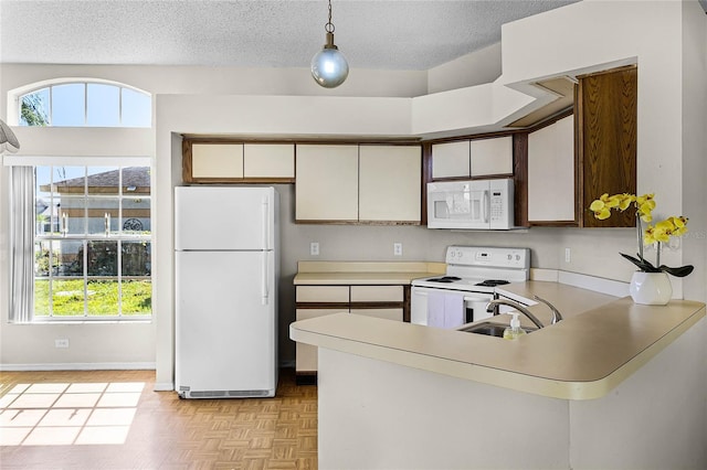 kitchen featuring white appliances, a peninsula, light countertops, a textured ceiling, and a sink