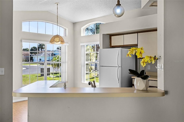 kitchen with pendant lighting, lofted ceiling, light countertops, freestanding refrigerator, and a textured ceiling