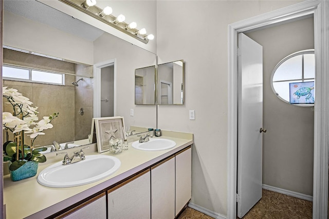 full bath featuring double vanity, baseboards, a sink, and tiled shower