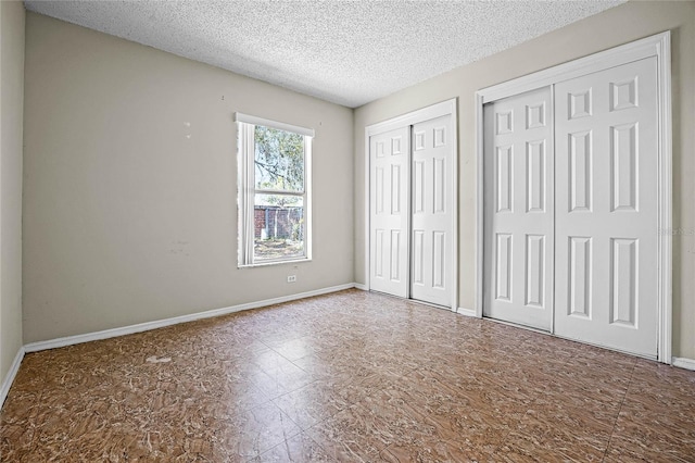 unfurnished bedroom featuring a textured ceiling, baseboards, and two closets