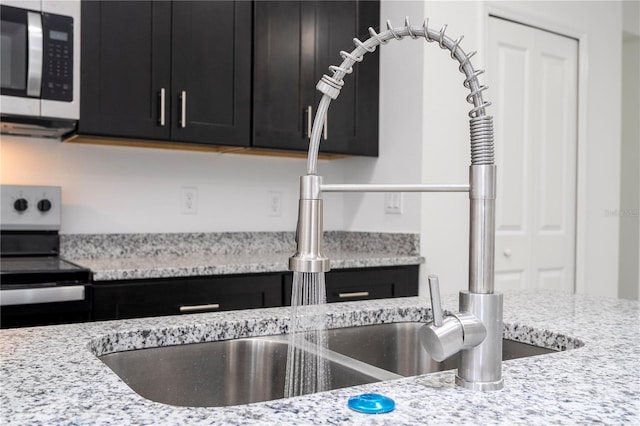 room details with light stone countertops, dark cabinets, appliances with stainless steel finishes, and a sink