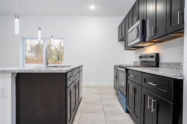 kitchen with baseboards, light tile patterned flooring, an island with sink, a sink, and appliances with stainless steel finishes