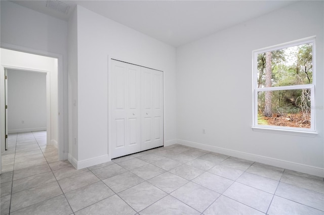 unfurnished bedroom with light tile patterned floors, visible vents, baseboards, and a closet