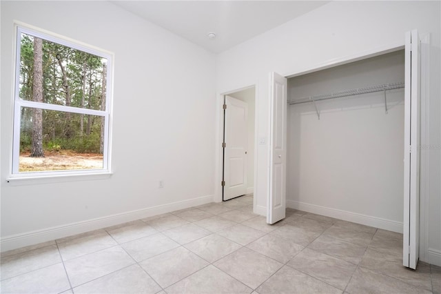 unfurnished bedroom with light tile patterned floors, multiple windows, baseboards, and a closet