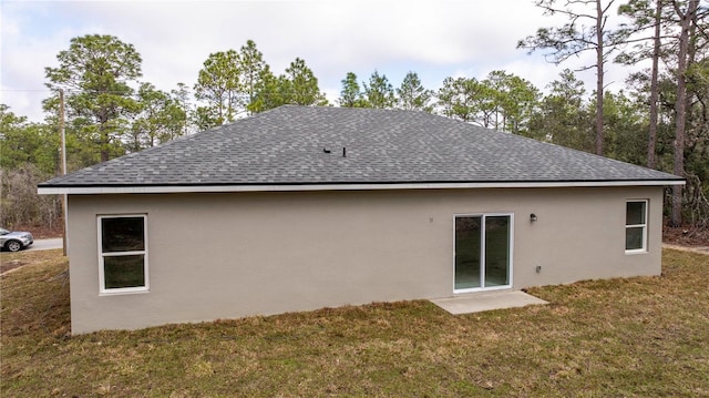 rear view of house with stucco siding, a shingled roof, and a yard