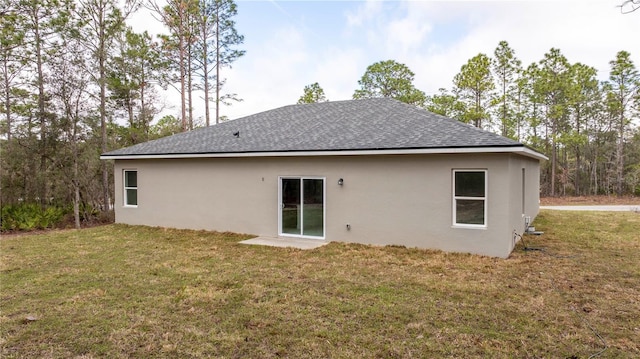 rear view of property featuring stucco siding, a yard, and roof with shingles