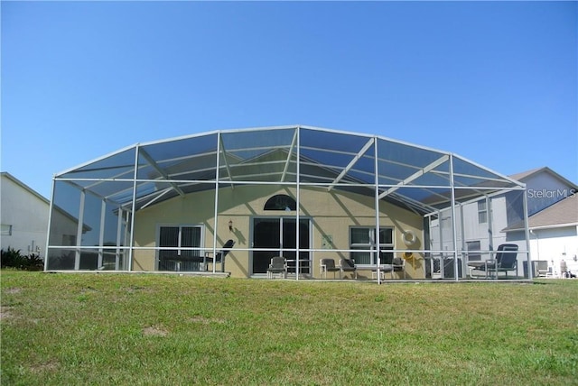 back of house with glass enclosure, a lawn, and stucco siding