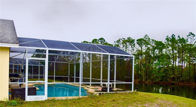 pool with glass enclosure, a water view, and a lawn