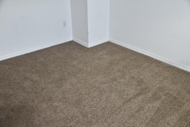 spare room featuring baseboards and dark carpet