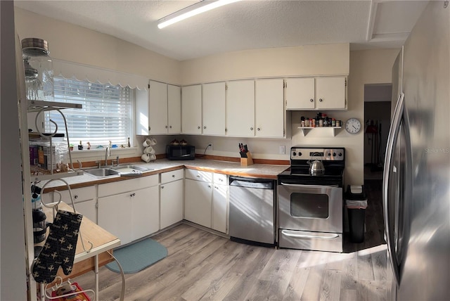 kitchen featuring light wood-style flooring, stainless steel appliances, light countertops, white cabinetry, and a sink