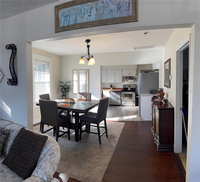 dining space featuring dark wood-style floors, a chandelier, visible vents, and a textured ceiling