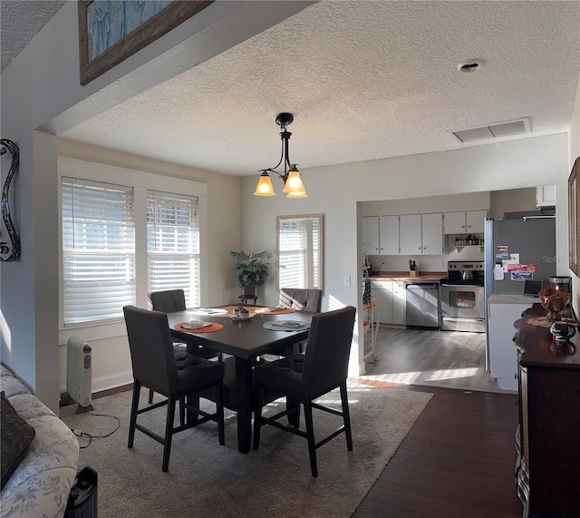 dining area featuring dark wood-style floors, visible vents, a textured ceiling, and an inviting chandelier