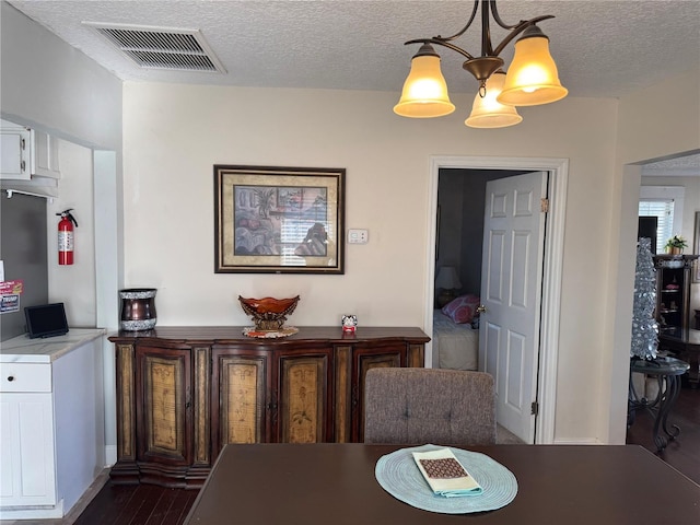 dining space featuring dark wood-style flooring, visible vents, a textured ceiling, and an inviting chandelier