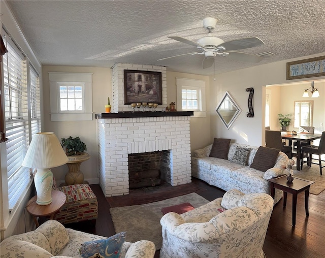 living area with a textured ceiling, dark wood-type flooring, ceiling fan with notable chandelier, and a fireplace