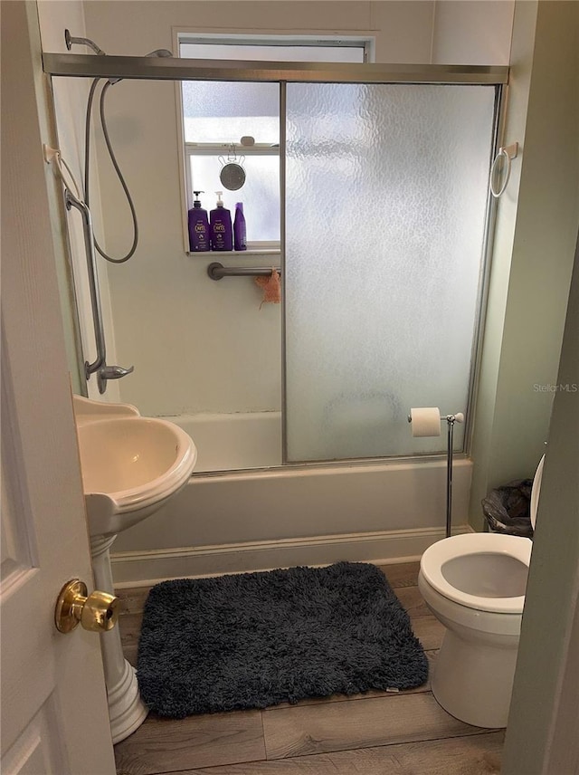 full bathroom featuring toilet, shower / bath combination with glass door, a sink, and wood finished floors