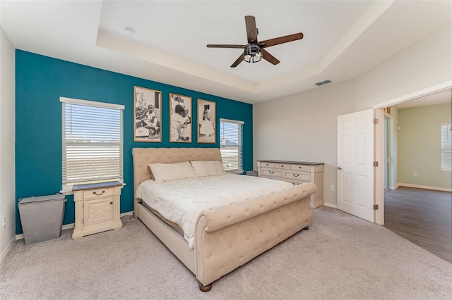 bedroom featuring a tray ceiling, light carpet, baseboards, and ceiling fan