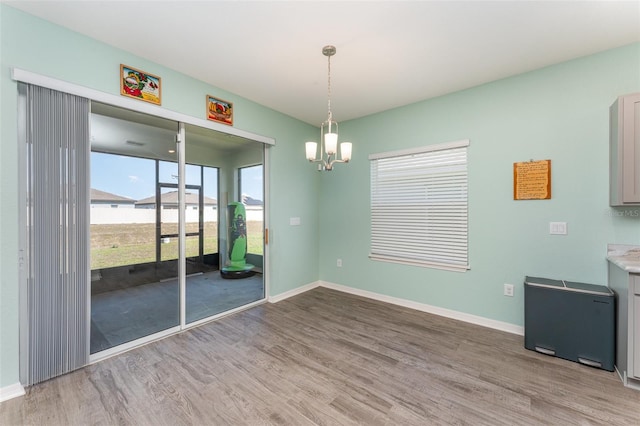 unfurnished dining area with wood finished floors, a chandelier, and baseboards