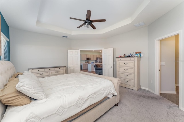 bedroom with a tray ceiling, baseboards, light colored carpet, and a ceiling fan