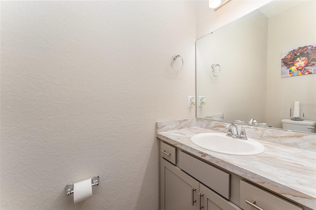 bathroom with vanity, toilet, and a textured wall