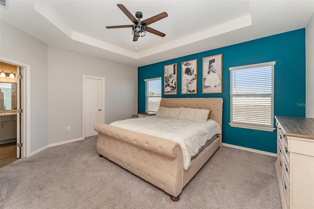 bedroom with a tray ceiling, light carpet, baseboards, and ensuite bathroom