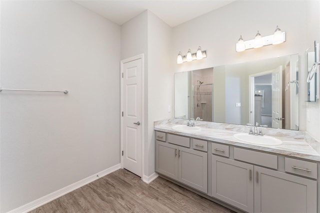 bathroom with a stall shower, wood finished floors, double vanity, and baseboards